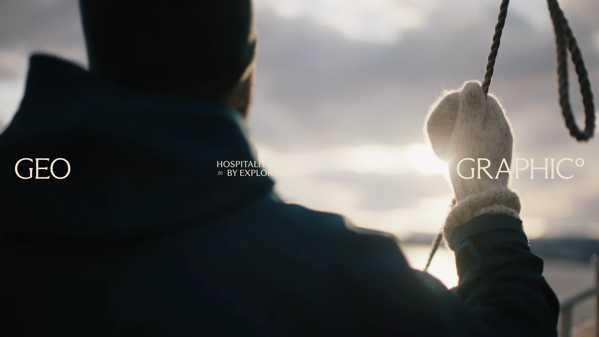 Geographic brand film still: a traveller in a knitted glove holding a rope at sunrise